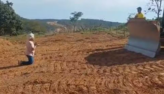 Idosa se ajoelha diante de máquina para tentar barrar obra de duplicação da GO-330